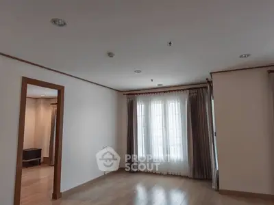 Spacious empty living room with wooden flooring and large windows with curtains.