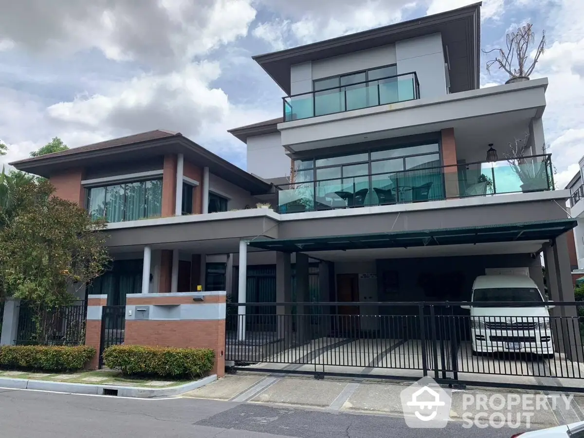 Modern two-story residence with expansive glass balcony, offering a blend of luxury and comfort with its contemporary architecture and lush surroundings.