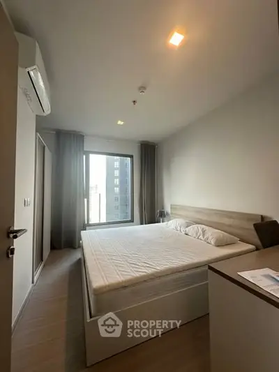 Modern bedroom with large window and minimalist design in urban apartment.