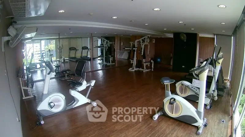 Spacious gym with modern exercise equipment and wooden flooring in a well-lit area.
