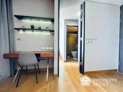 Modern study area with sleek desk and chair, adjacent to a bathroom with wooden flooring.