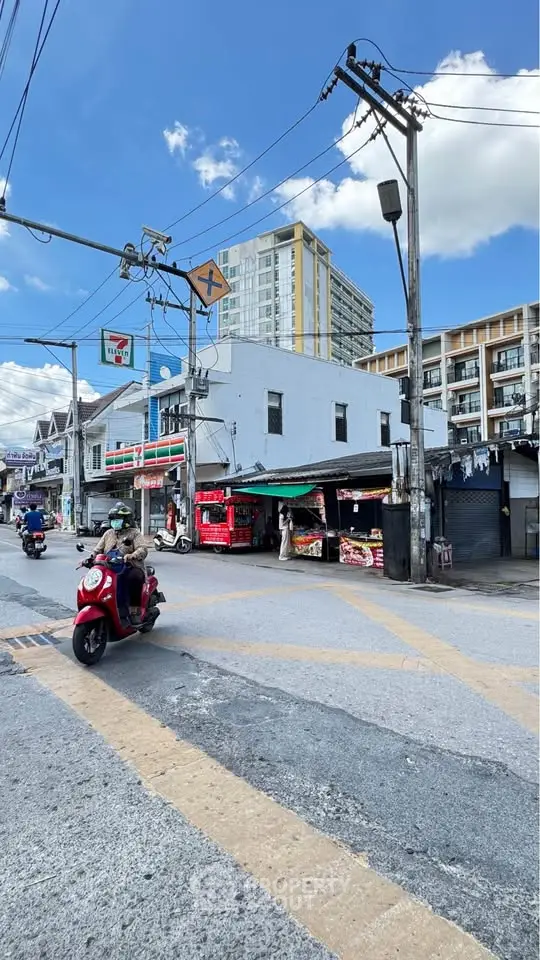 Urban street view with residential buildings and local shops under a clear blue sky.