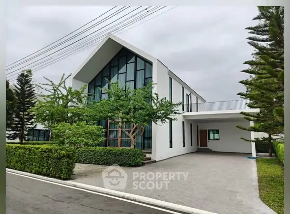 Modern two-story house with large windows and driveway in lush green setting.