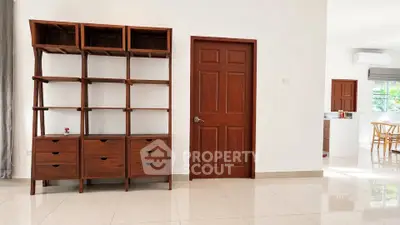 Spacious modern living area with wooden shelving and door, featuring sleek tiled flooring and natural light.