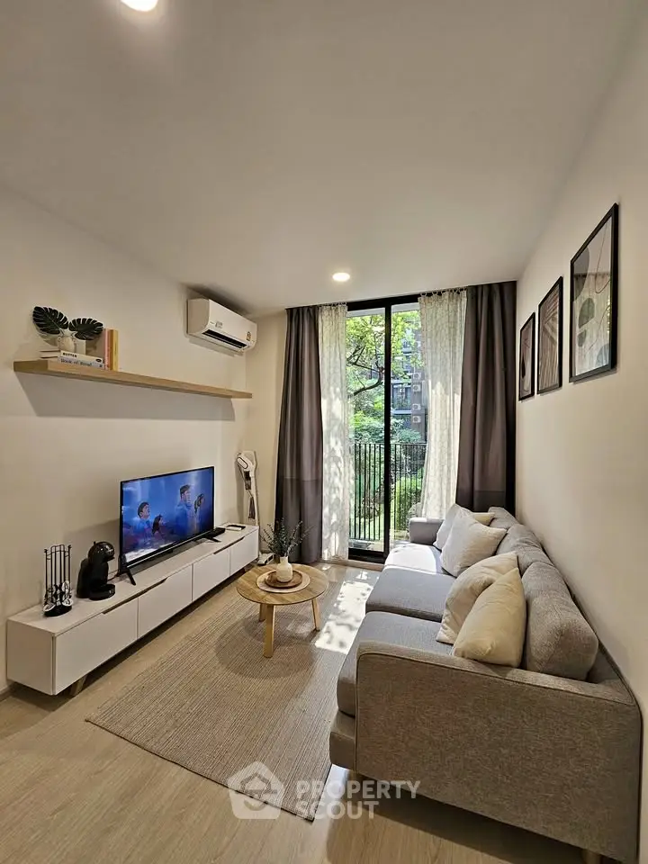 Modern living room with cozy sofa, wall-mounted TV, and large window overlooking greenery.