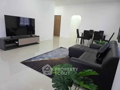 Modern living room with sleek black sofa and large TV, open dining area