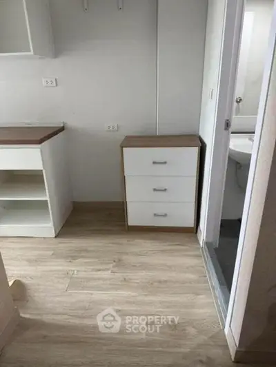 Compact kitchen area with wooden flooring and adjacent bathroom entrance.