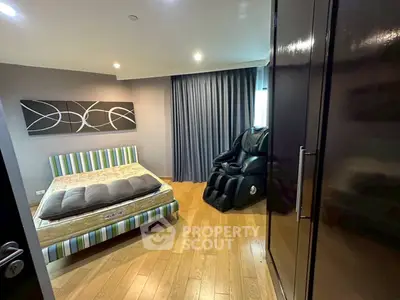 Spacious bedroom with modern decor and massage chair, featuring wooden flooring and stylish curtains.