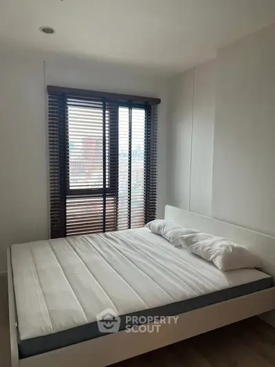 Modern bedroom with large window and city view, featuring a minimalist bed and sleek blinds.