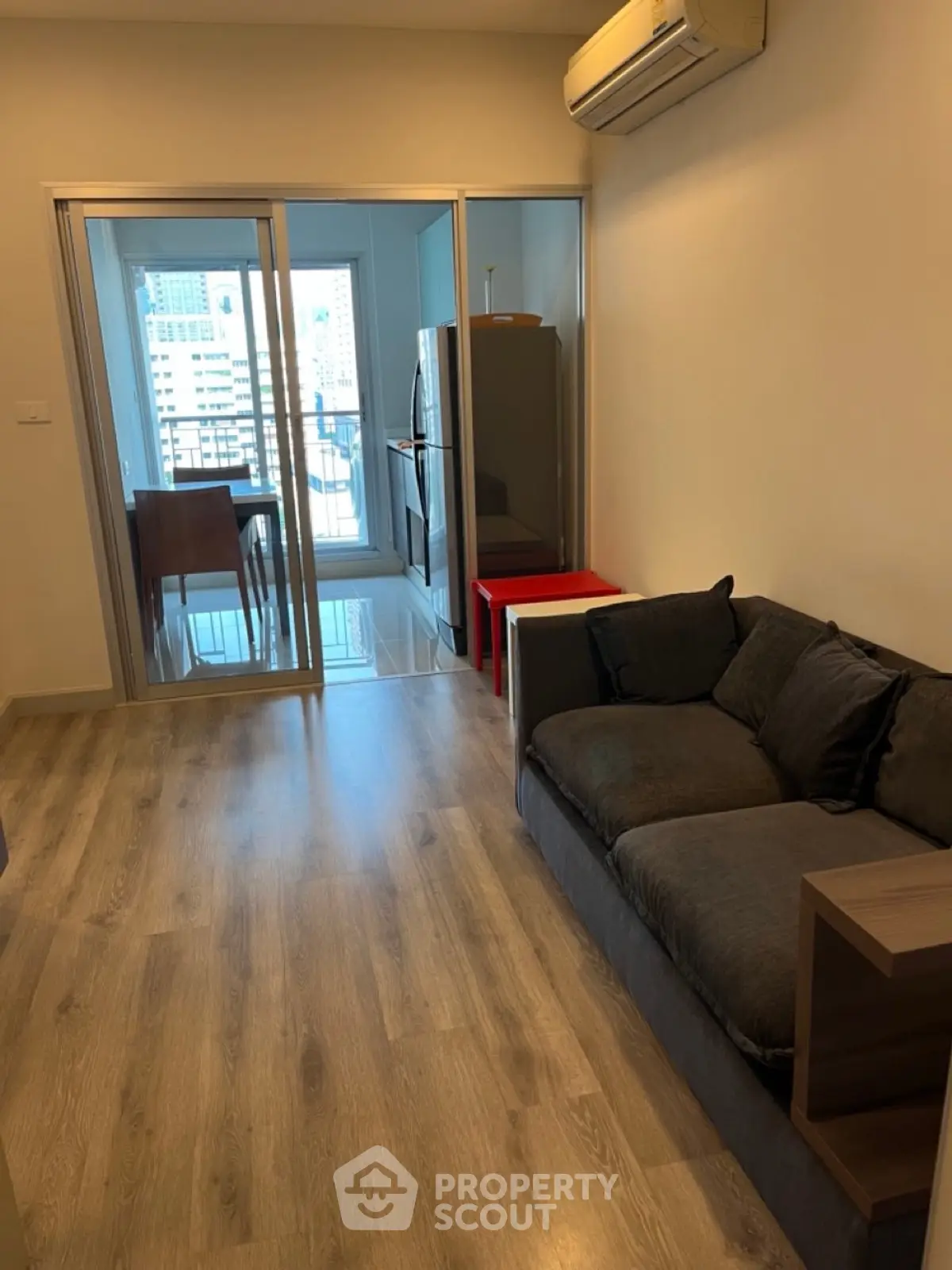 Modern living room with wooden flooring and glass doors leading to a dining area with city view.