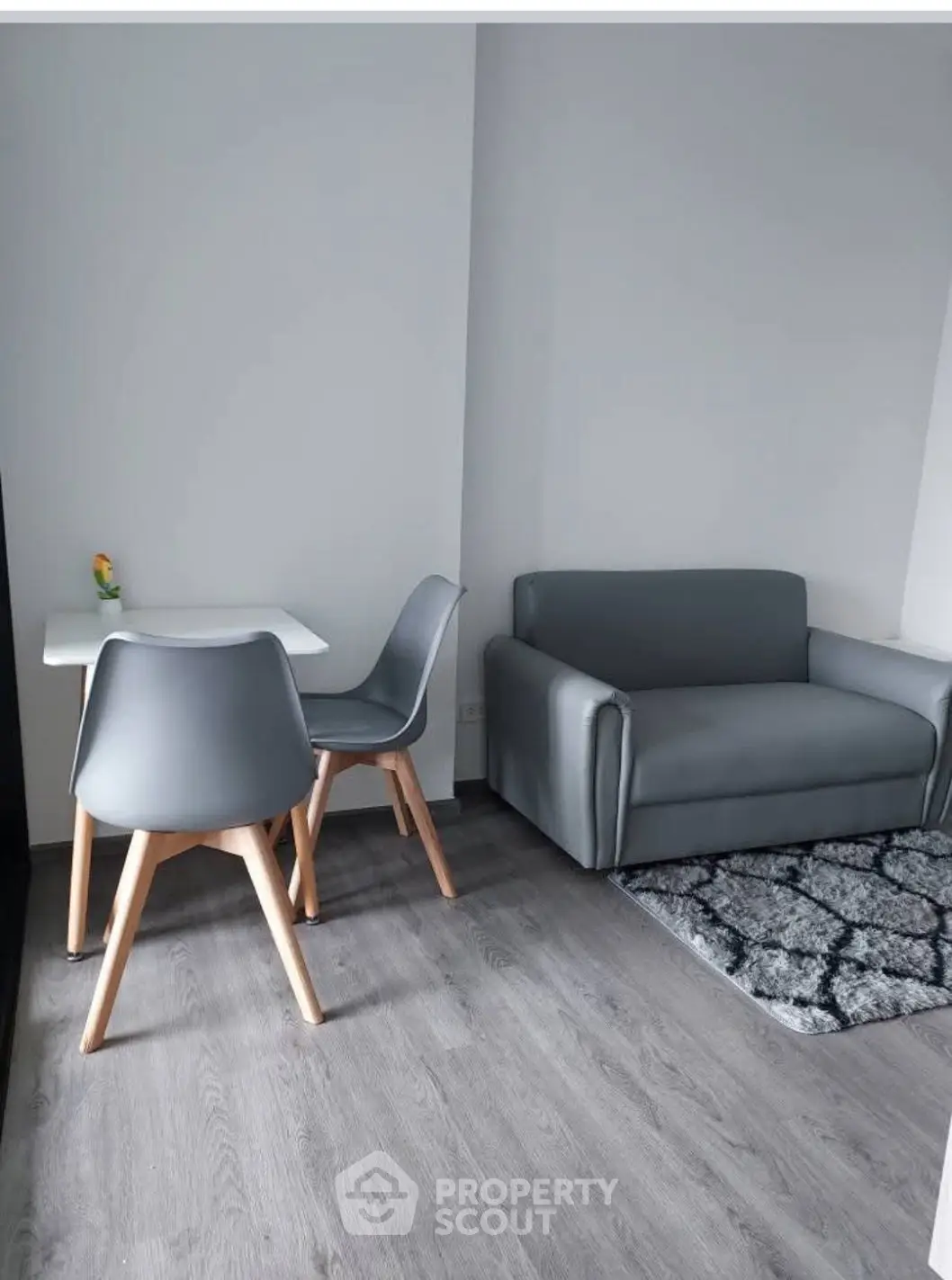 Modern minimalist living room with gray sofa and dining set on wooden flooring.