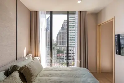Modern bedroom with large window offering stunning city view in high-rise apartment.