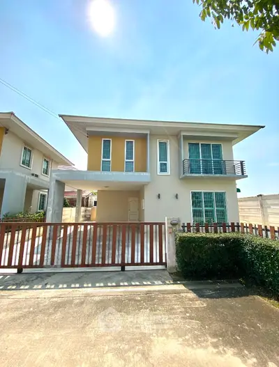 Modern two-story house with balcony and gated driveway in sunny neighborhood.