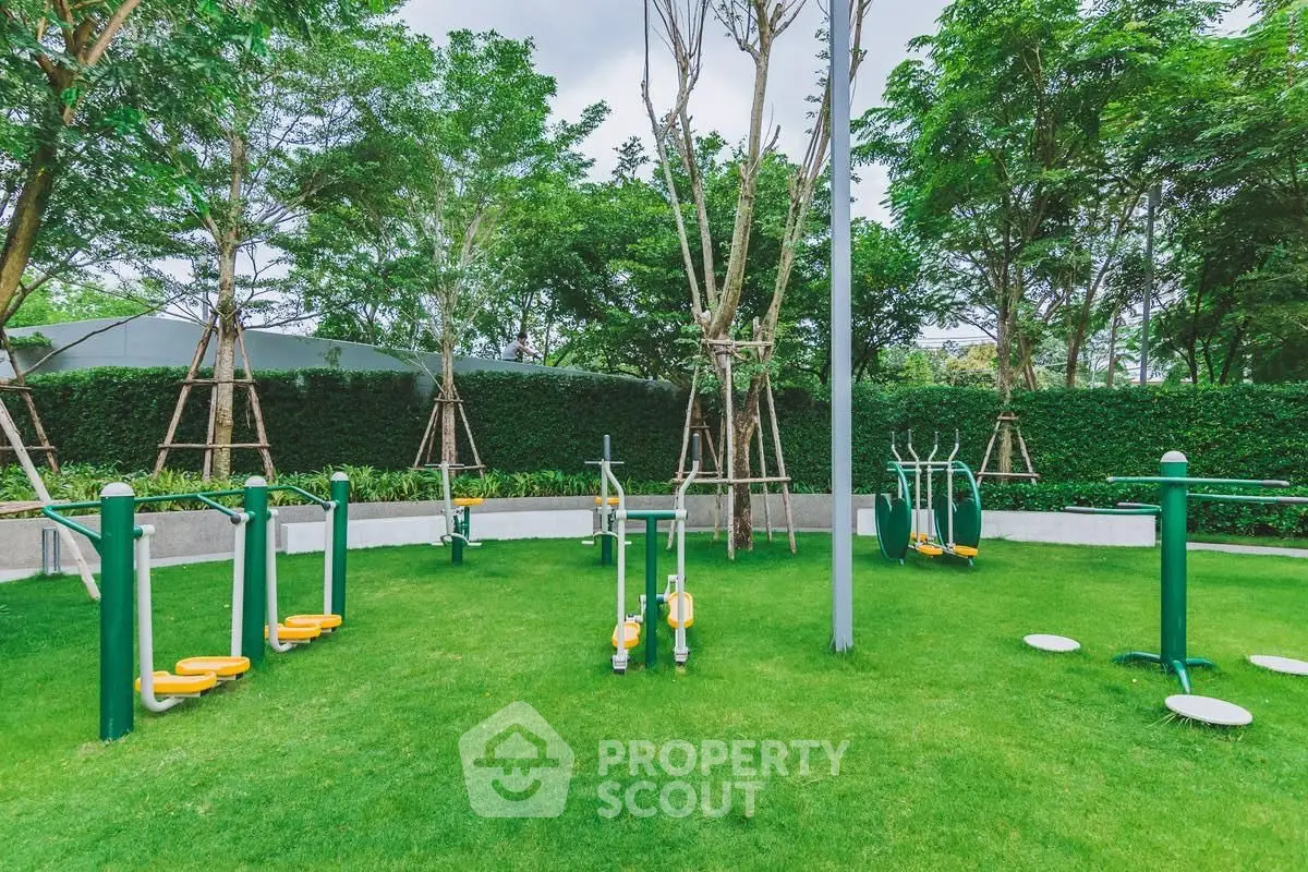 Lush green outdoor gym area with modern exercise equipment and trees.