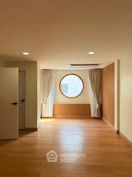 Spacious modern room with wooden flooring and unique circular window design.