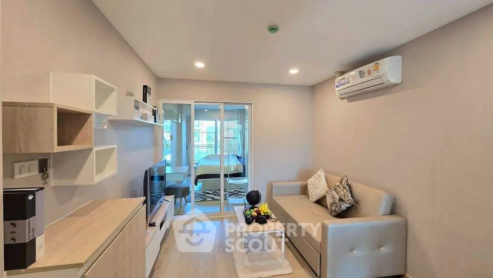 Modern living room with sleek furniture and air conditioning, featuring a view into a cozy bedroom.