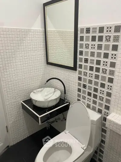 Modern bathroom with stylish black and white tile design and elegant vessel sink.