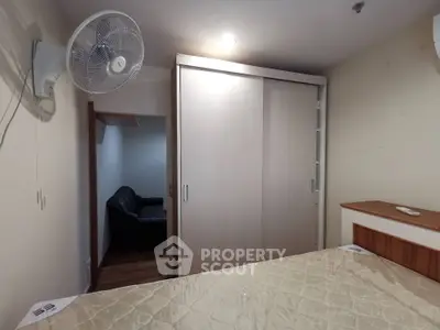 Cozy bedroom with wardrobe and wall-mounted fan, adjacent to a small living area.