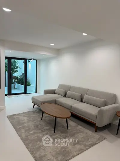 Modern living room with sleek gray sofa and stylish coffee table, opening to a lush garden view.