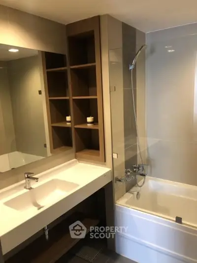 Modern bathroom with sleek fixtures and built-in shelving, featuring a bathtub and large mirror.