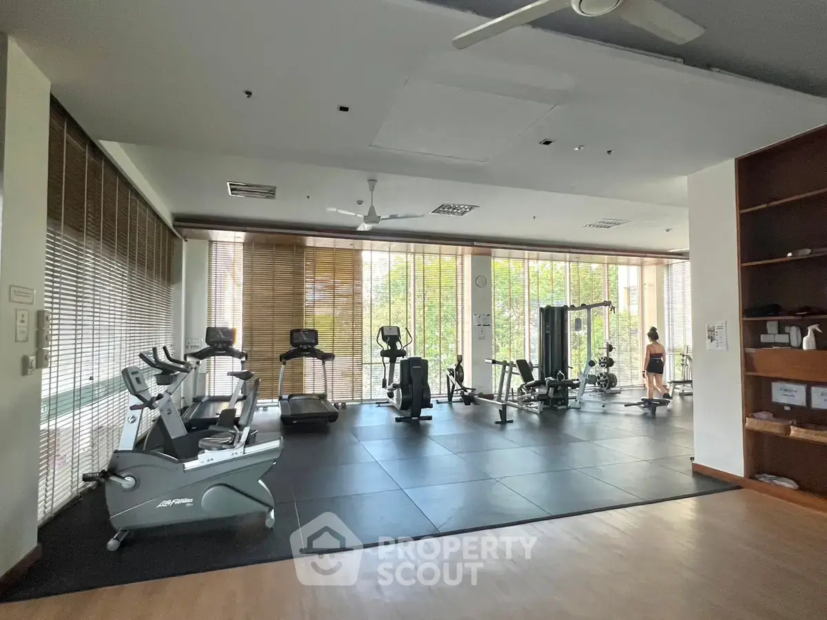 Spacious gym with modern equipment and large windows in a residential building.