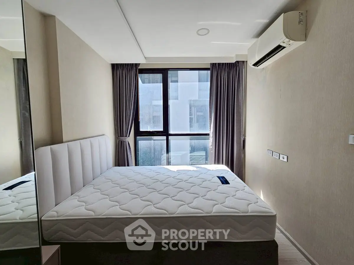 Modern bedroom with large window and air conditioning unit, featuring a comfortable mattress.