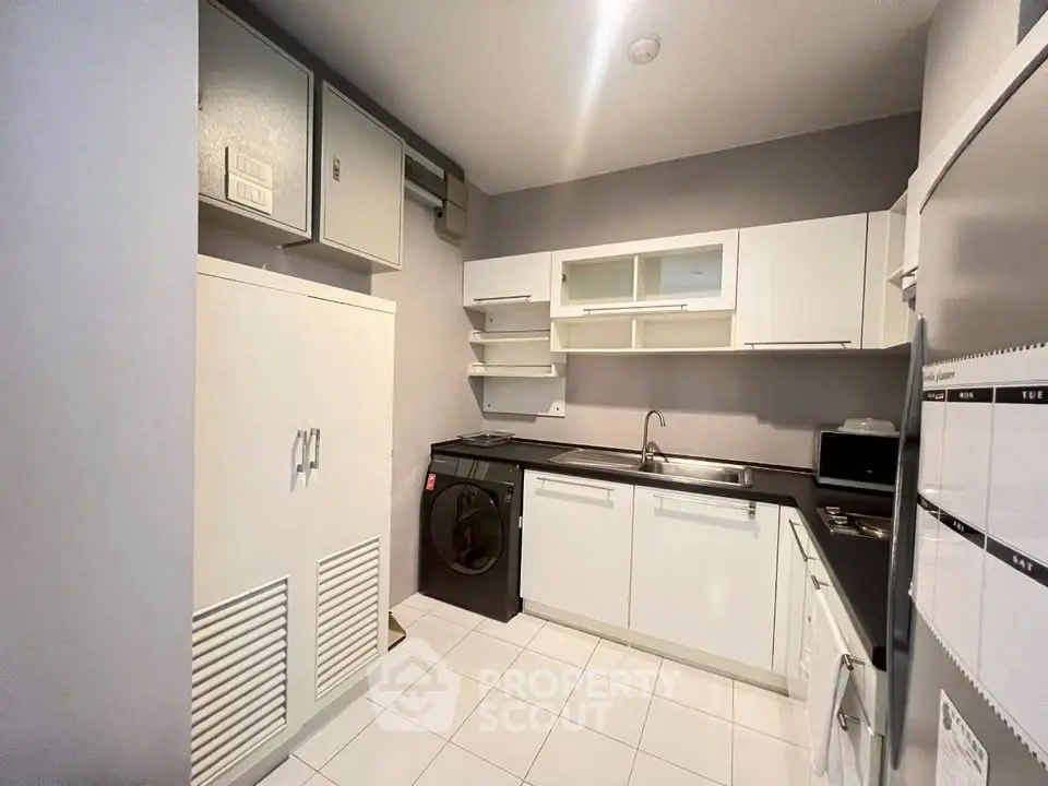 Modern kitchen with sleek white cabinets and built-in appliances, featuring a washing machine and ample storage.
