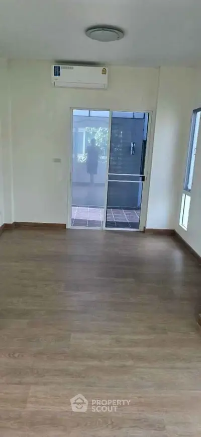 Spacious empty room with wooden flooring and large glass door leading to balcony.
