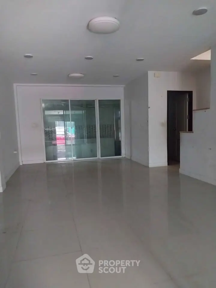 Spacious empty room with sleek tiled flooring and glass sliding doors, ideal for modern living.