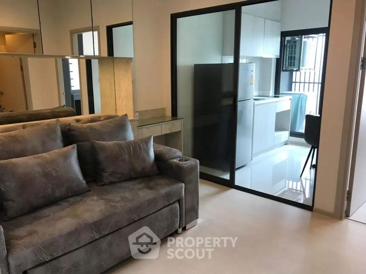 Modern apartment with sleek kitchen and cozy living area, featuring a stylish sofa and glass partition.