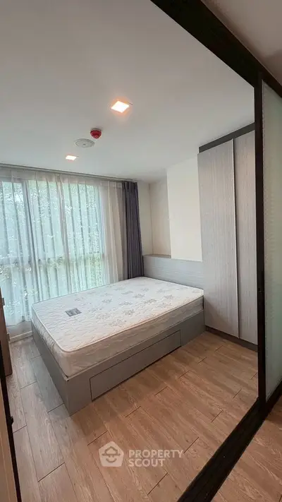 Modern bedroom with large window and wooden flooring in a stylish apartment.