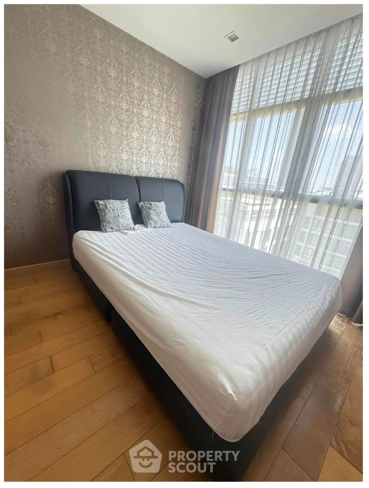 Spacious bedroom with elegant decor and large window offering natural light.