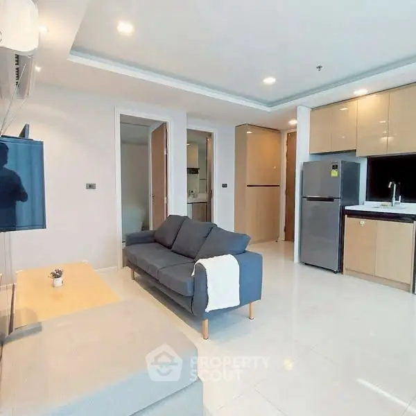 Modern living room with open kitchen, featuring sleek appliances and cozy seating area.