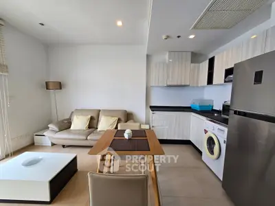 Modern open-layout living room with kitchen, featuring sleek furniture and appliances.