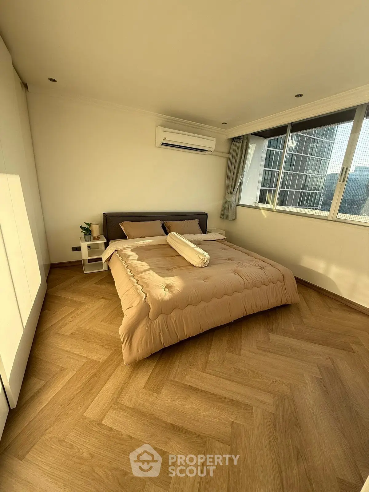 Spacious bedroom with large windows and modern decor in a high-rise apartment.