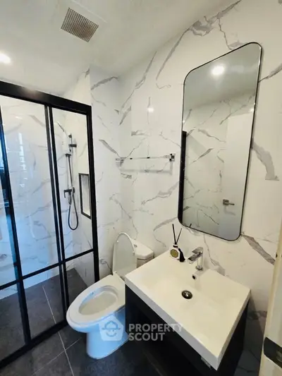 Modern bathroom with sleek design, featuring a glass shower enclosure and elegant marble walls.