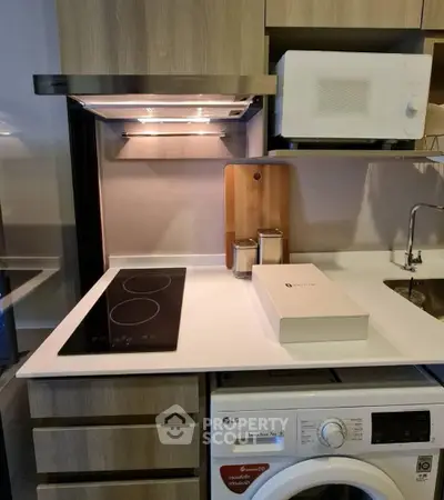 Modern kitchen with sleek induction cooktop, microwave, and washing machine in compact layout.