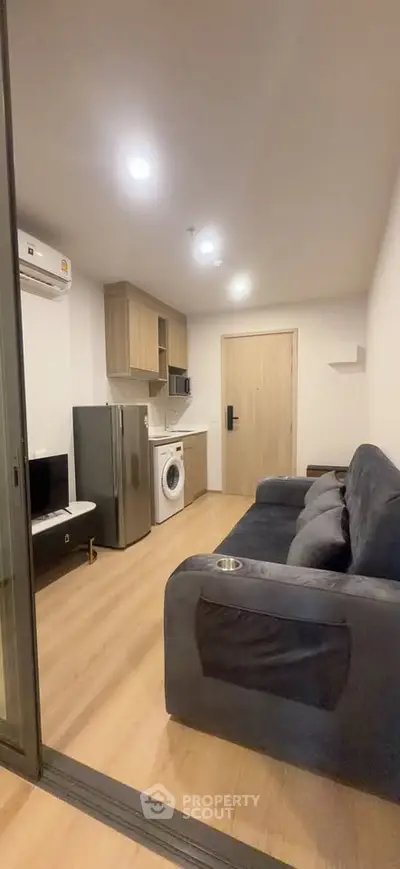 Modern living room with sleek furniture and integrated kitchen appliances in a cozy apartment.