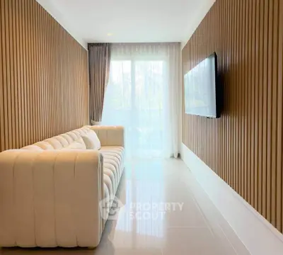 Modern living room with elegant wood paneling and plush white sofa, featuring a wall-mounted TV and large window.