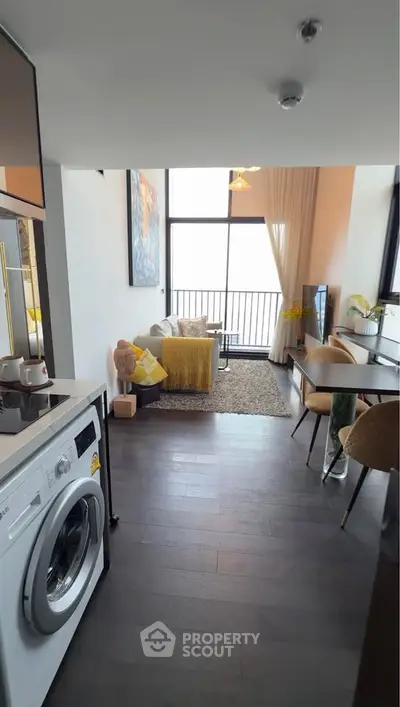 Modern living room with washing machine, cozy seating, and balcony view in stylish apartment.