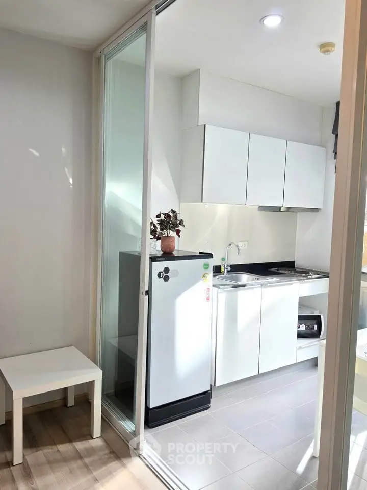 Modern compact kitchen with sleek white cabinets and sliding glass door, perfect for urban living.
