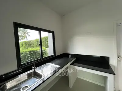 Modern kitchen with sleek black countertops and large window overlooking lush greenery.