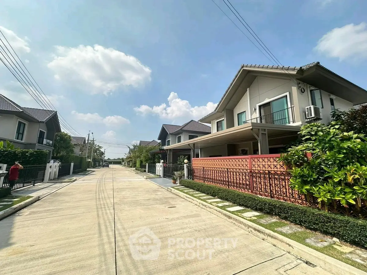 Charming suburban street with modern detached houses and lush greenery under a clear blue sky.