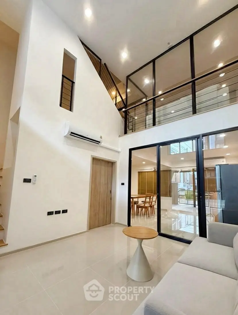 Modern living room with high ceiling and glass balcony overlooking dining area.