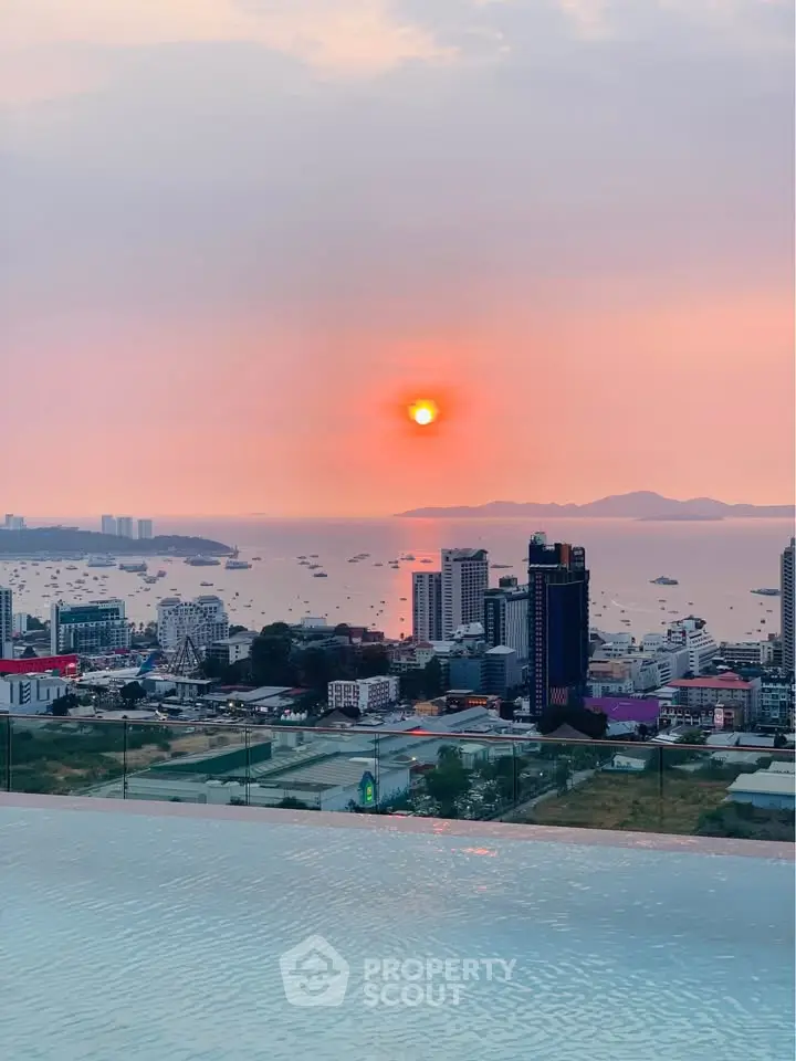 Stunning rooftop view of city skyline and ocean at sunset, featuring infinity pool.