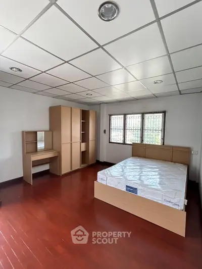 Spacious bedroom with wooden flooring and modern furniture, featuring a large bed and wardrobe.