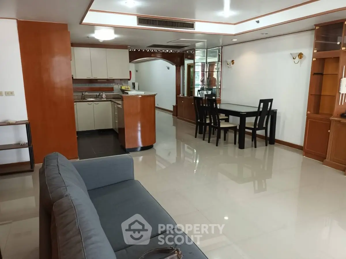 Spacious open-plan living room with modern kitchen and dining area, featuring sleek furniture and polished floors.