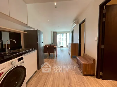 Modern apartment interior with kitchen and living area, featuring wooden flooring and natural light.