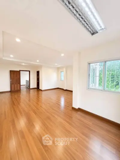 Spacious empty living room with wooden flooring and large window view.