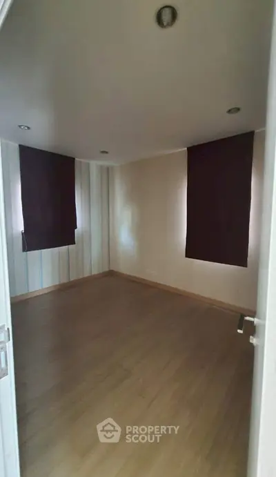 Spacious empty room with wooden flooring and dark curtains, ideal for customization.